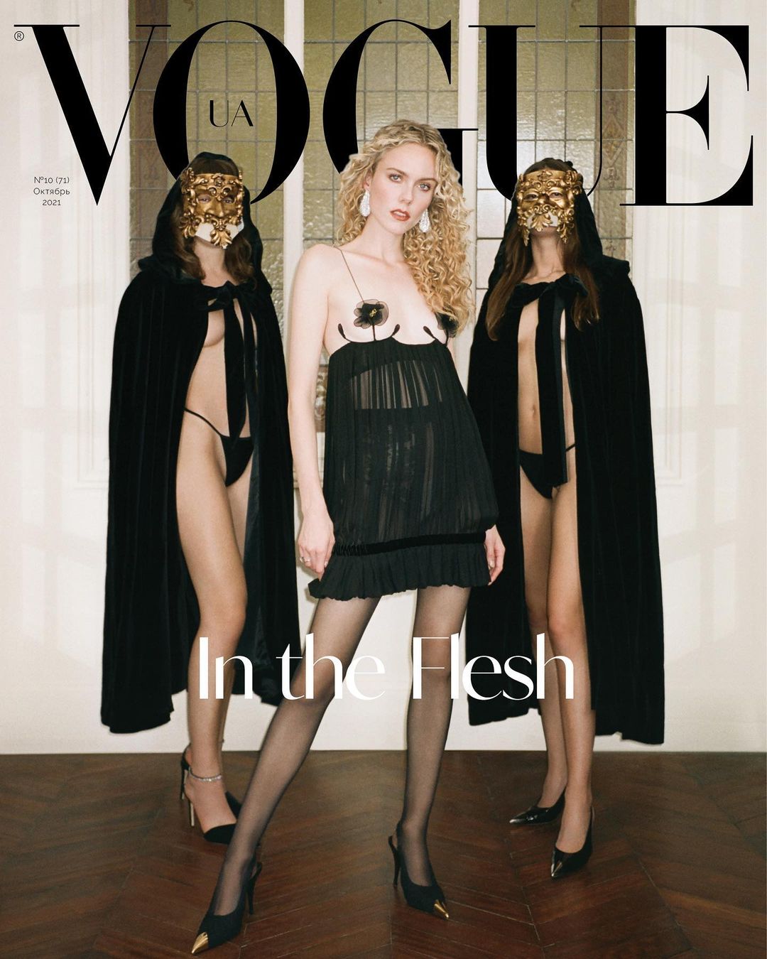 Vogue UA cover featuring a fair-skinned woman in a black dress and heels, flanked by two masked figures in black cloaks and heels.