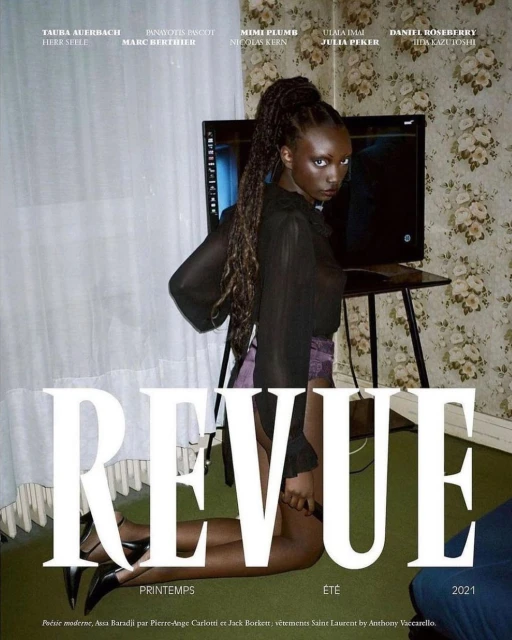 Magazine cover featuring a Black woman with long braids kneeling in front of a television, wearing a sheer black blouse and purple skirt.