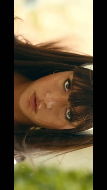 Close-up of a brown-haired woman with bangs looking directly at the camera with neutral expression in front of a light background.
