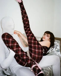 Woman in plaid tights posed with a person in a white full-body suit against a foil backdrop