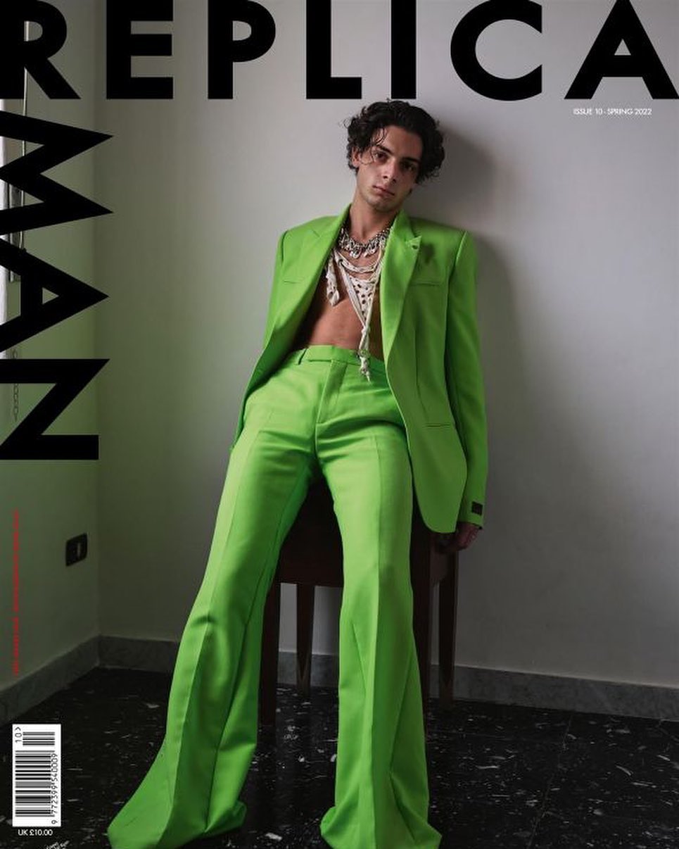 Fashion magazine cover featuring a male model in a green suit and layered necklaces, posing against a neutral wall.
