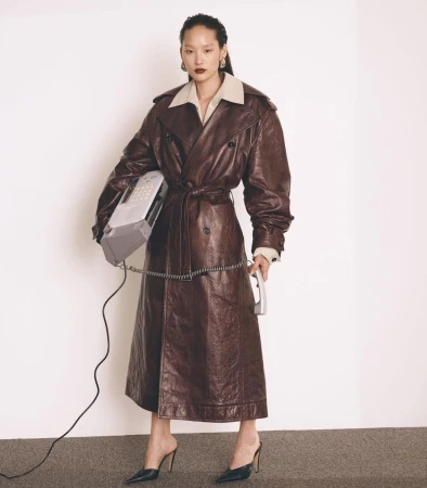 Model wearing a brown leather trench coat holding a vintage landline telephone in a studio portrait by Pieter Hugo