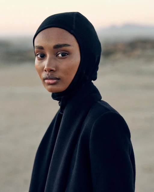 Portrait of a Black female adult with neutral expression, wearing a black balaclava and jacket against a neutral outdoor background.