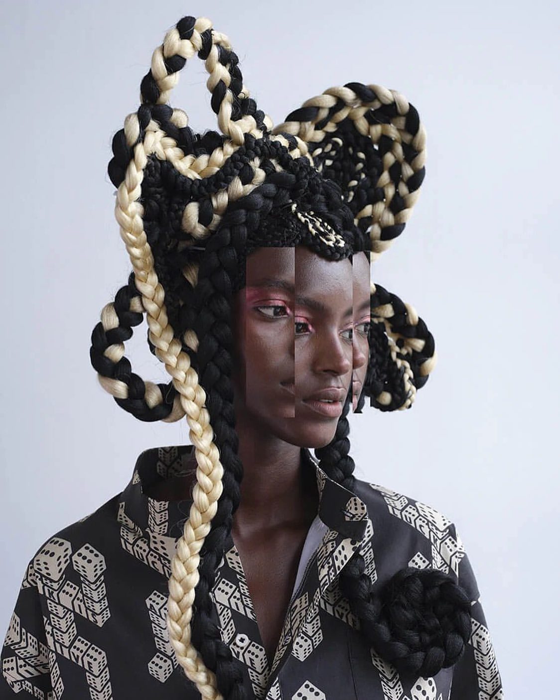 Fashion portrait of an African woman with a sculptural black and white braided hairstyle, wearing a patterned jacket against a white backdrop.