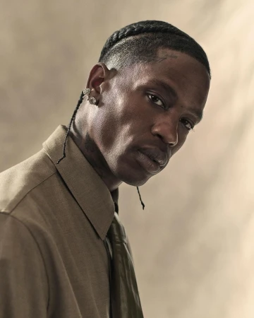Portrait of an adult man with cornrow braids, wearing a khaki button-down shirt and tie, against a neutral studio backdrop with soft lighting.