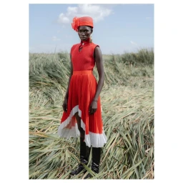 Model in red dress and matching hat standing among tall green reeds outdoors by photographer Pieter Hugo