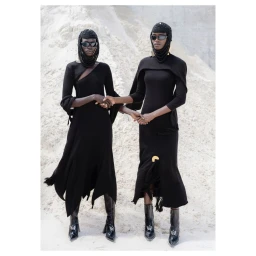 Two models in black dresses and beaded headcoverings standing together against a pale sandy background by Pieter Hugo