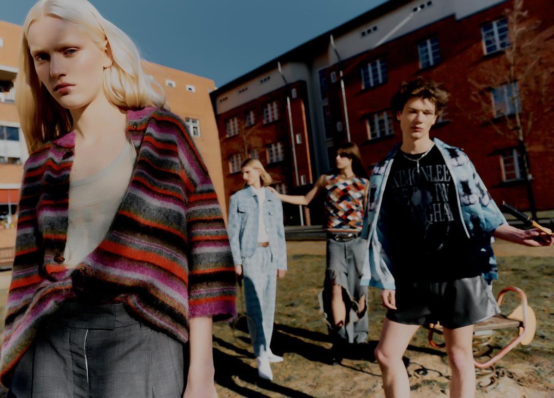Fashion editorial featuring a group of young adults in vintage-inspired clothing, posing outdoors against a backdrop of residential buildings.