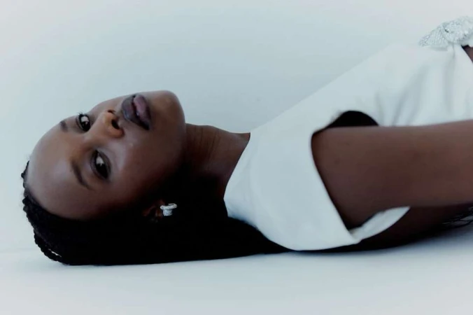 Portrait of a Black woman in a white dress lying on a plain white background, photographed by Pietro Groff.