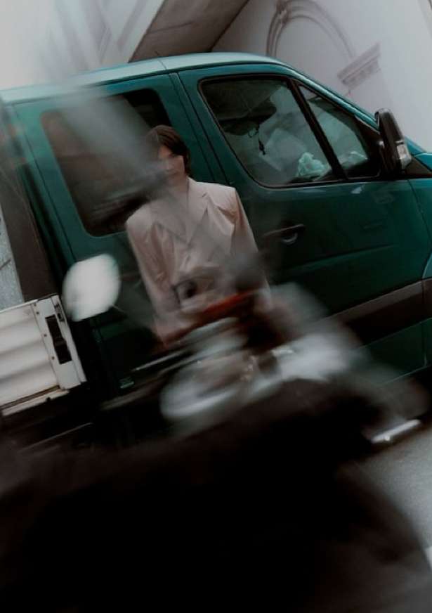Green delivery van in motion with blurred background and foreground. An individual is sitting inside the vehicle with light shining.