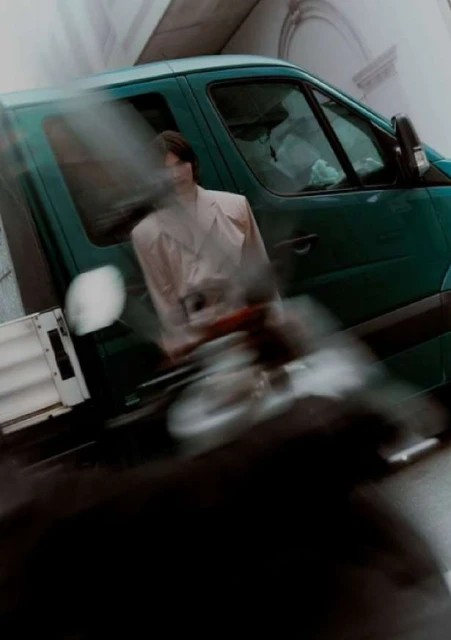Green delivery van in motion with blurred background and foreground. An individual is sitting inside the vehicle with light shining.