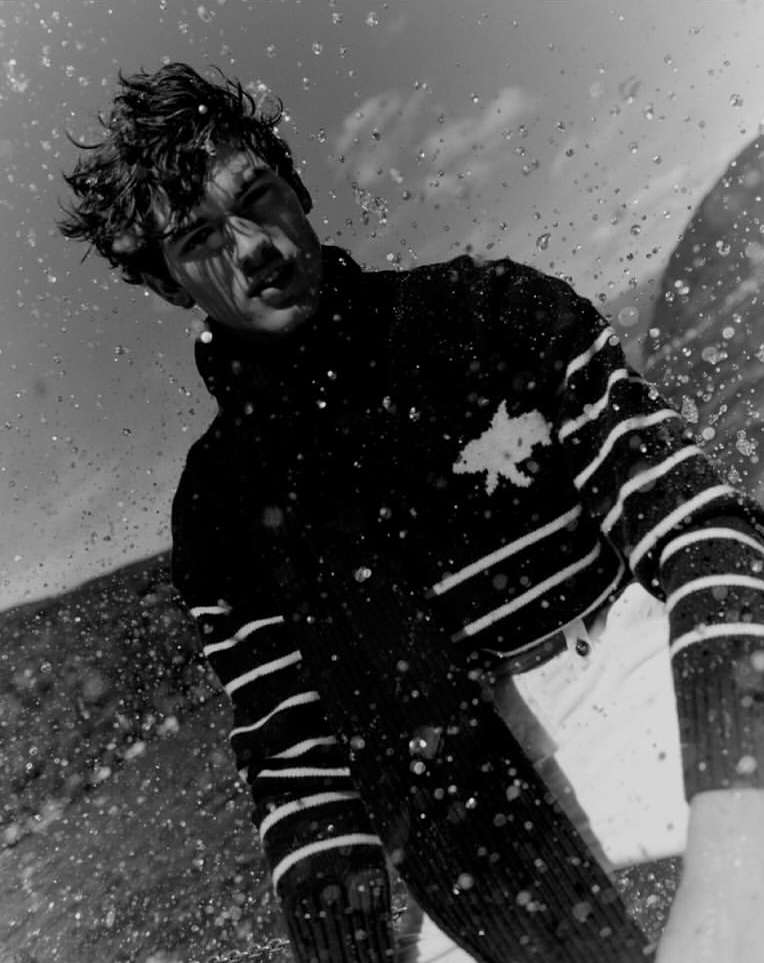 Monochrome portrait of a young adult male in a striped sweater, captured in motion with water droplets and a low angle.