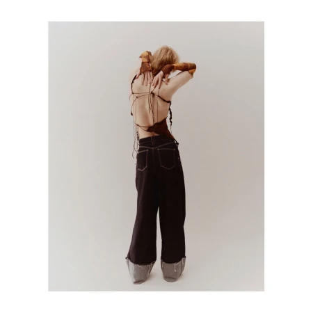 Model photographed from behind wearing a strappy backless top, dark baggy trousers, and fingerless sleeves