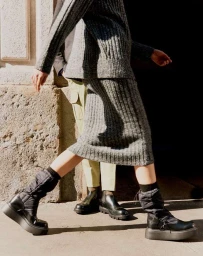Low-angle shot of a person in a grey ribbed knit skirt suit and black puffer boots walking outdoors in Milan.