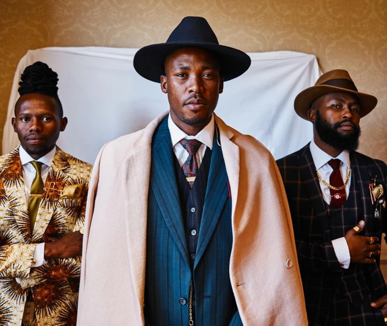Three stylish Black men pose in patterned suits and hats, creating a fashion-forward, striking image with high-end style and elegant backdrops.