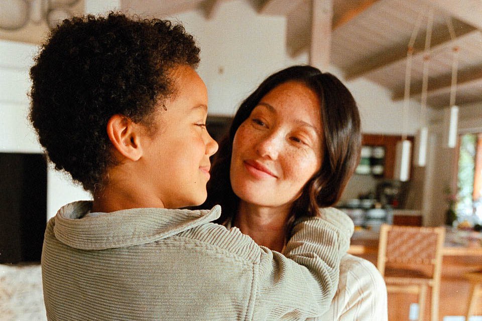 Portrait of a woman and child embracing indoors, featuring a warm color palette and soft lighting, creating a cozy and familial atmosphere.