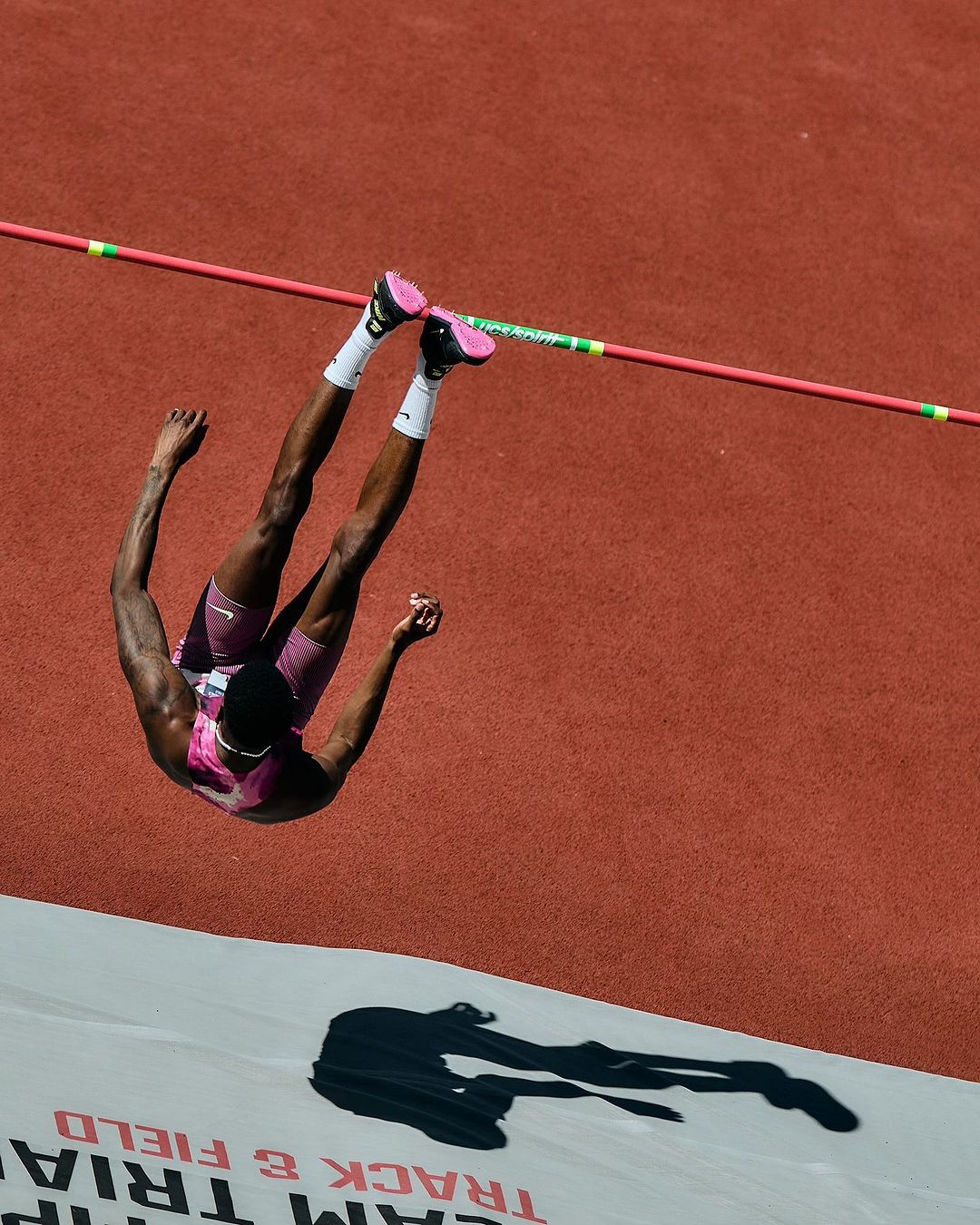 High angle view of an African American athlete clearing the high jump bar at an outdoor track and field event on a sunny day.