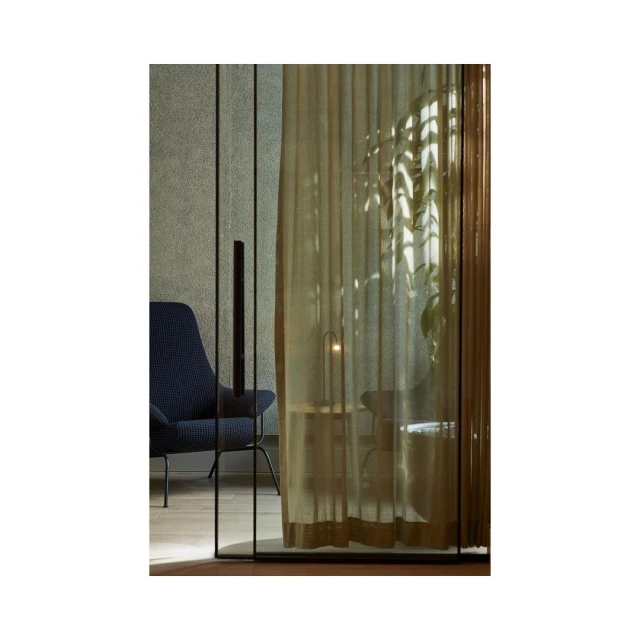 Interior view of a modern living room featuring a blue armchair, sheer curtains, and soft lighting, creating a cozy, stylish atmosphere.