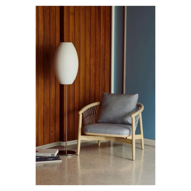 Living room interior featuring a modern wooden chair with a gray cushion and a tall white lamp, complemented by a wooden wall.