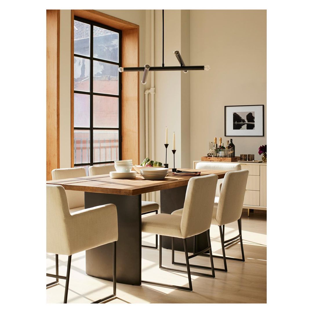 Contemporary dining room interior featuring a wooden table, upholstered chairs, modern chandelier, and window with natural light.
