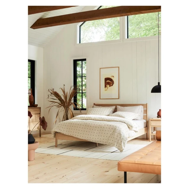 Bedroom interior with a light wood bed featuring a patterned duvet, complemented by neutral walls and natural lighting from windows.