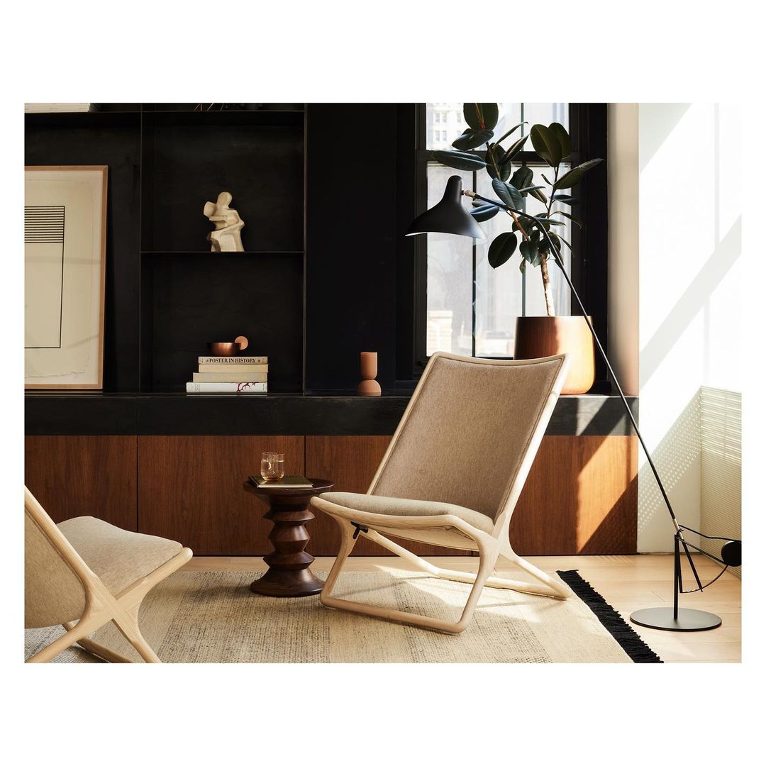 Interior design featuring two light beige lounge chairs, dark wood side table with a glass, and a floor lamp in a modern room.