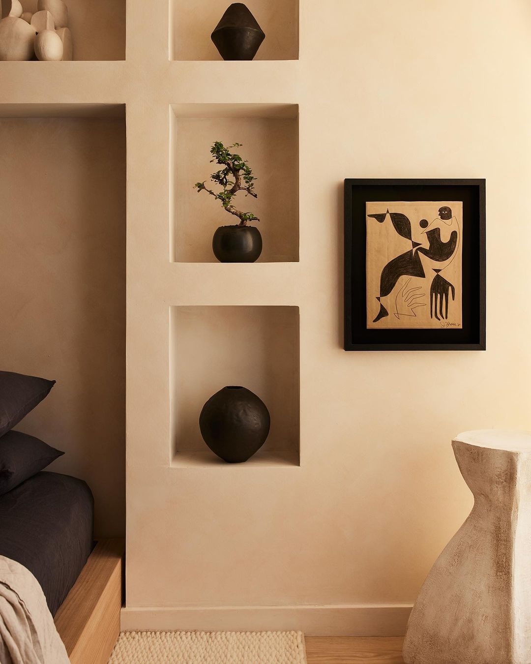Interior with wall niches featuring vases and plants, a framed abstract art piece, and a minimalist side table in a neutral color palette.
