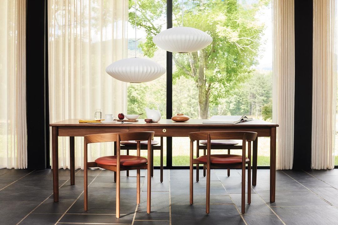 Dining room interior featuring a wooden table with chairs, lit by two white pendant lights and natural light from a large window.