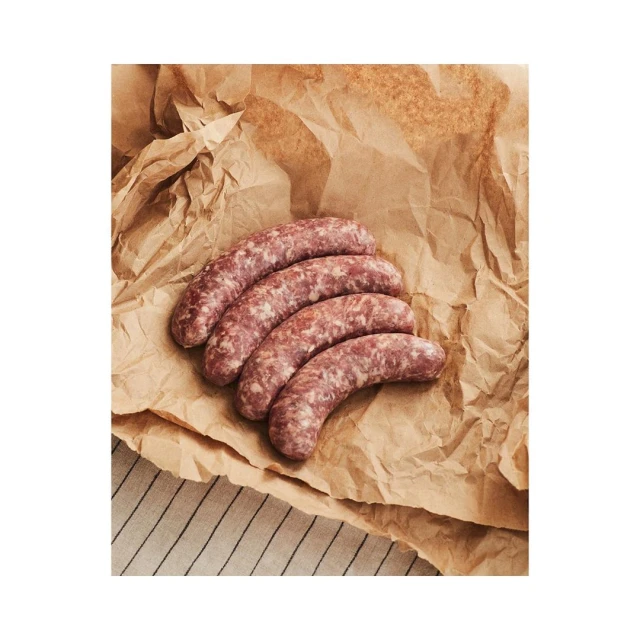 Close-up view of four raw sausages on a brown, crinkled paper surface with a striped textile in the background.