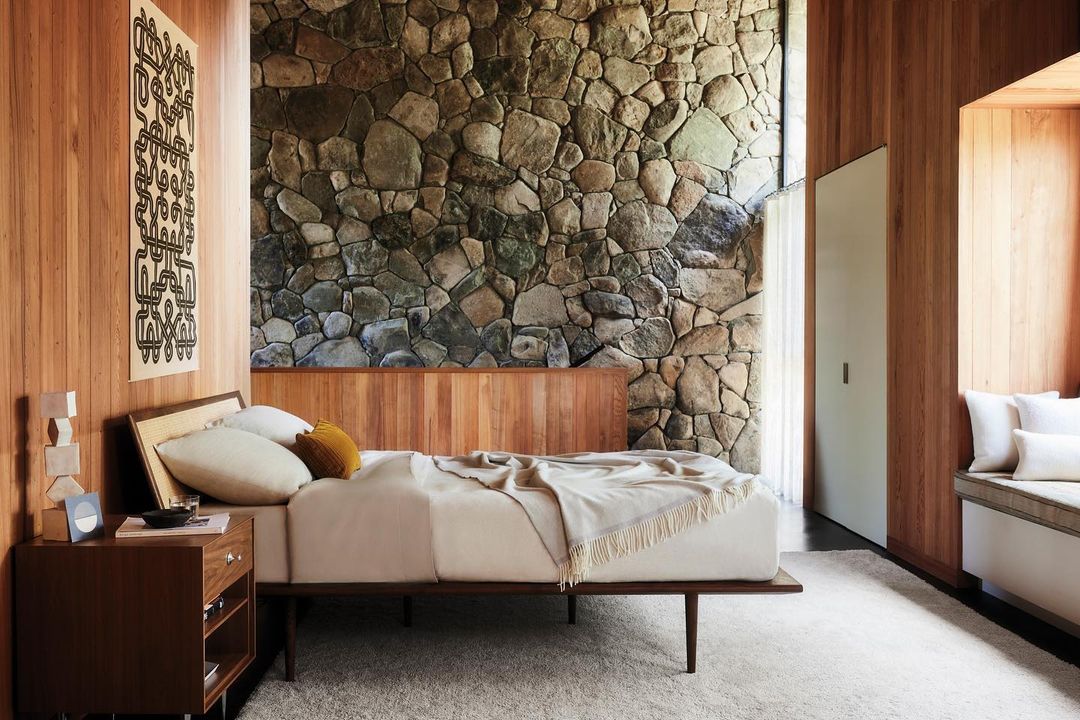 Bedroom interior featuring a bed with stone accent wall, wood paneling, nightstand, and a neutral color palette, creating a cozy atmosphere.