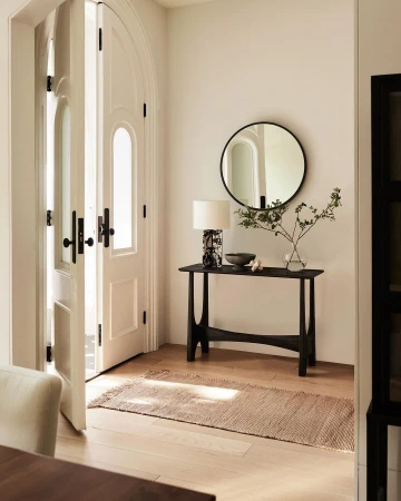 Interior entryway featuring white doors, a black console table with a lamp, and a round mirror against a light neutral wall.