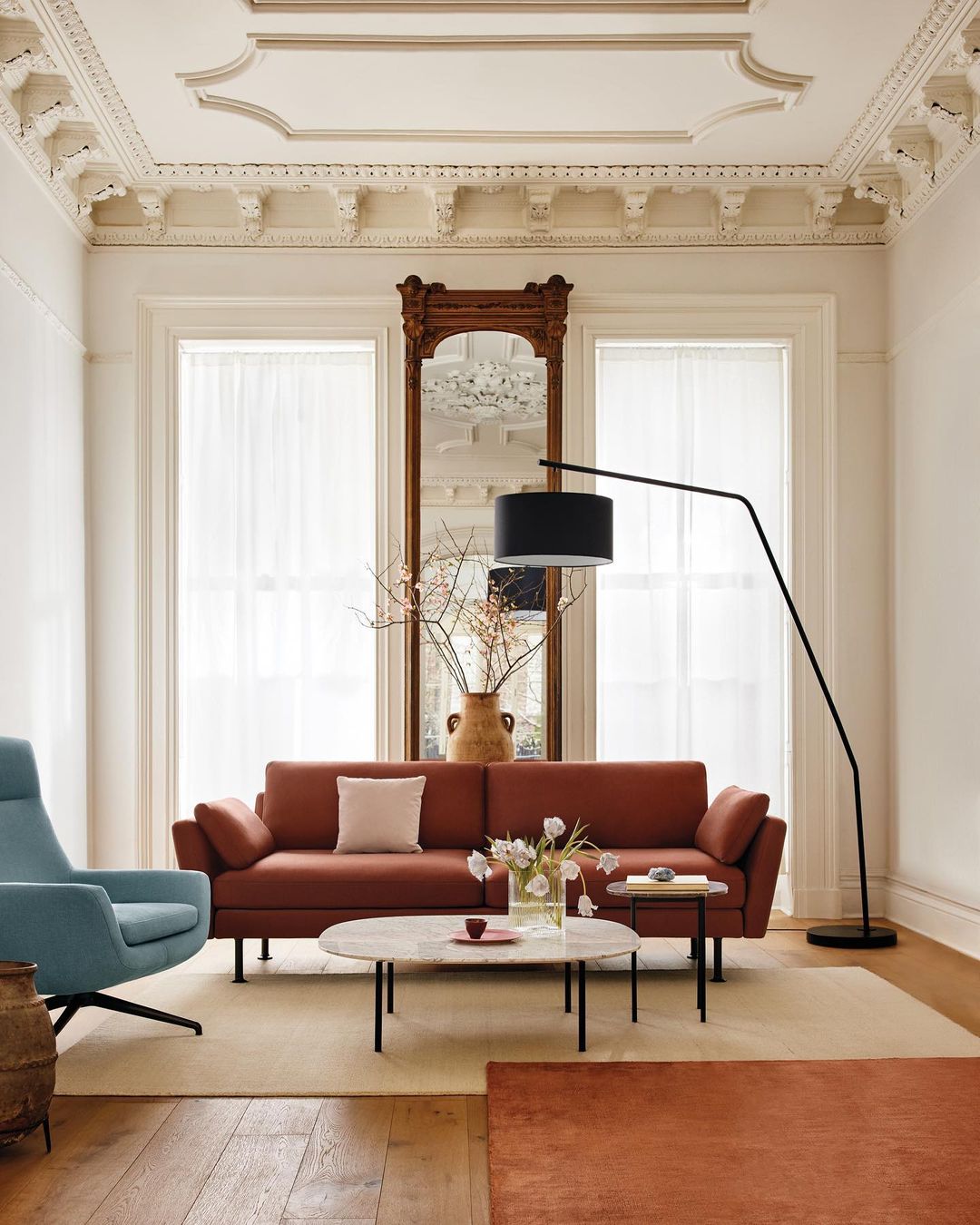Living room interior with terracotta sofa, marble coffee table, blue chair, black floor lamp, and neutral tones in a classically designed space.