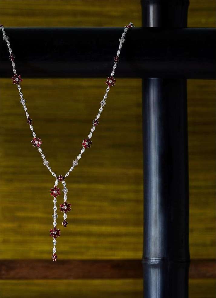 Elegant necklace with red and white floral gems displayed against a backdrop of black textured metal and blurred yellow fabric.