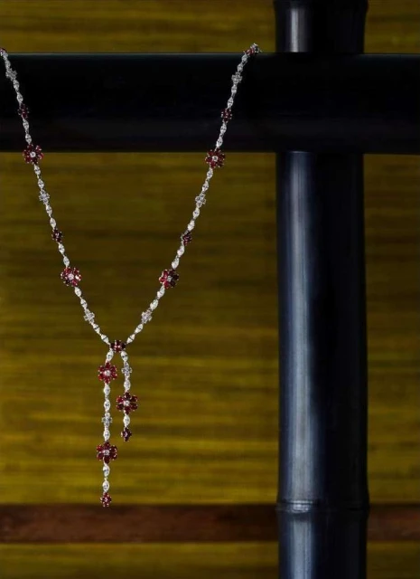 Elegant necklace with red and white floral gems displayed against a backdrop of black textured metal and blurred yellow fabric.
