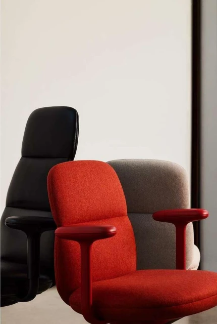 Three office chairs in black, red, and grey with fabric upholstery and ergonomic design are arranged in front of a white wall.