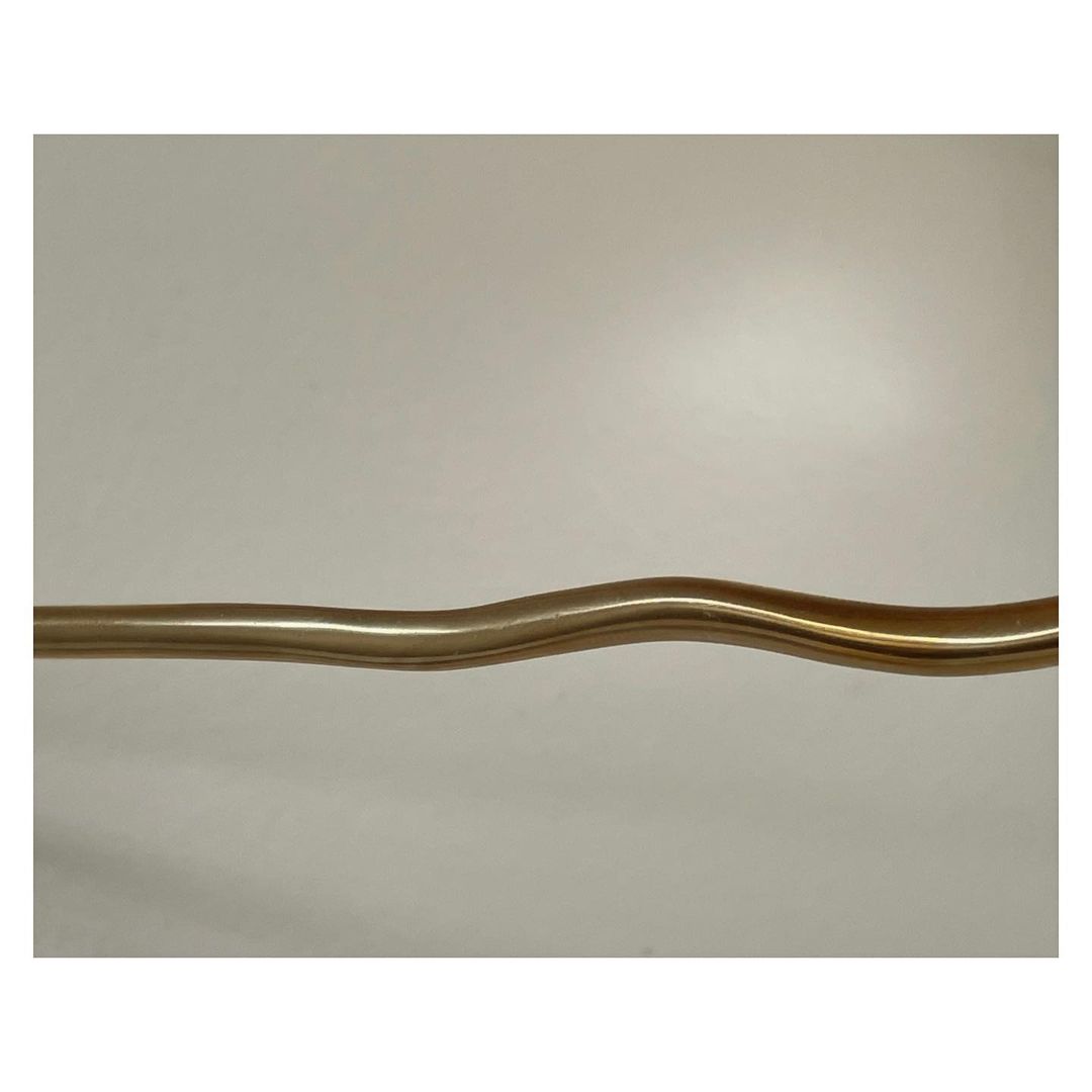 Abstract studio shot of a curved brass tube against an off-white background, with a simple, modern aesthetic, and soft lighting.