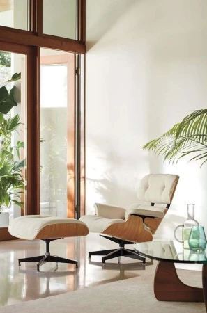 Eames-style chair and ottoman in a bright, modern living room near an open window. Interior design with natural light and simple decor.