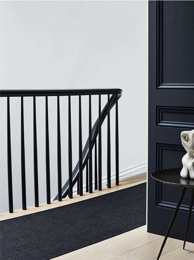 Interior view showcasing a staircase with a black railing, a dark runner rug on light wood stairs, a dark blue door, and modern table.