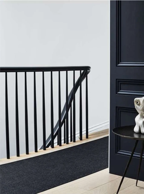 Interior view showcasing a staircase with a black railing, a dark runner rug on light wood stairs, a dark blue door, and modern table.