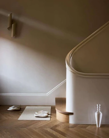 Minimalist interior design featuring a staircase with white banister, wooden floor, and light-colored slippers and vase, creating a serene ambiance.