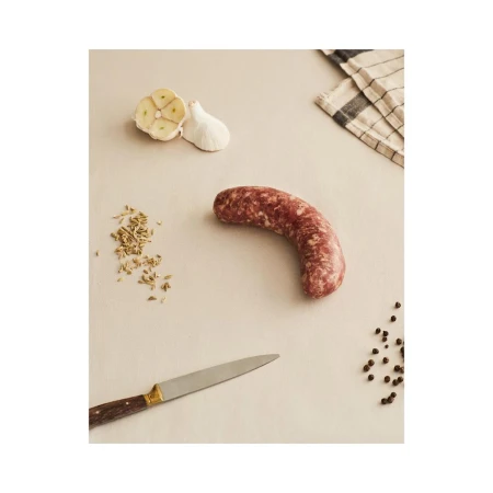 Overhead studio shot of raw sausage, garlic cloves, spices, peppercorns, and knife on a tan surface, perfect for culinary projects.