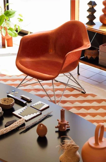 Orange mid-century modern molded plastic chair on a metal base, set on a rug indoors next to a black table with decorative objects.