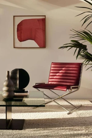 Red leather lounge chair on a textured white rug with a glass coffee table, vase, and abstract wall art.
