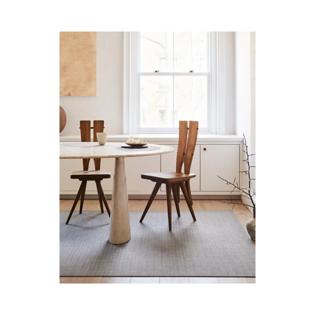 Dining room interior featuring a round table set with dishware, complemented by two stylish wooden chairs and a gray rug.