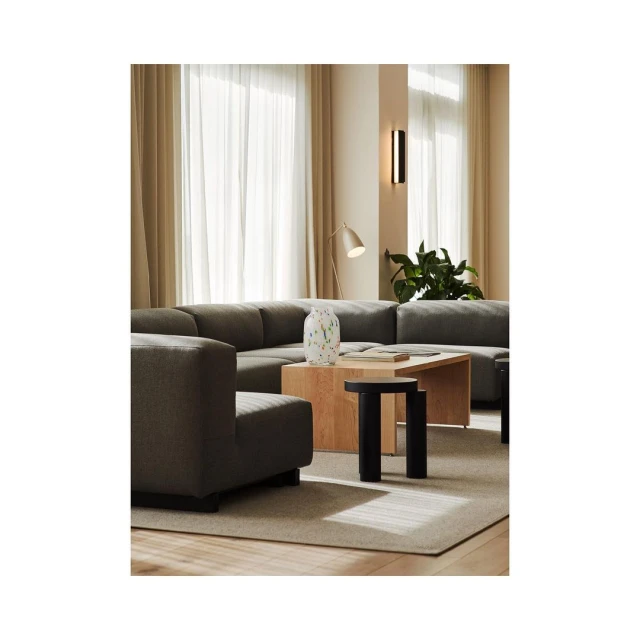 Living room interior featuring a grey sectional sofa, wooden coffee table, patterned vase, and black side table, illuminated by natural light.