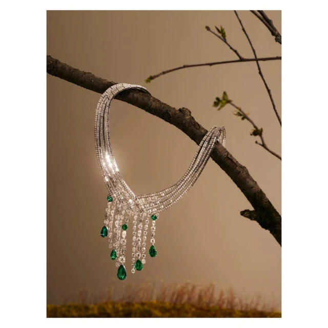 Elegant diamond and emerald necklace draped on a branch, showcased in a jewelry fashion still life with neutral studio background and soft lighting.