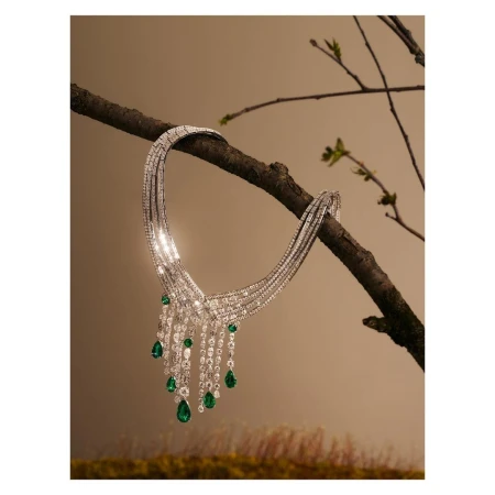 Elegant diamond and emerald necklace draped on a branch, showcased in a jewelry fashion still life with neutral studio background and soft lighting.