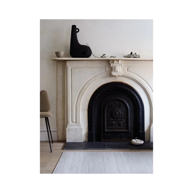 Interior featuring a black vase on a white fireplace mantel, a beige chair, and a light gray rug, showcasing modern home decor.