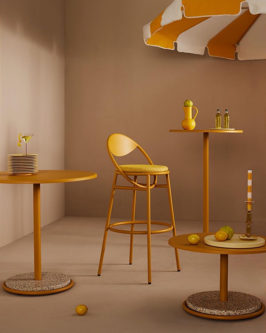 Stylish indoor scene with yellow bar stool and tables, decorated with cocktail, lemons, and striped parasol, creating a bright, summery atmosphere.