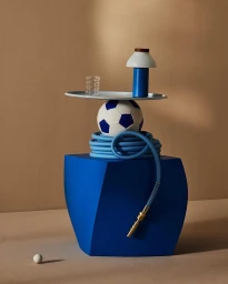 A sculptural still life of stacked blue objects including a block, a coiled hose, a soccer ball, a tray, and a small lamp.